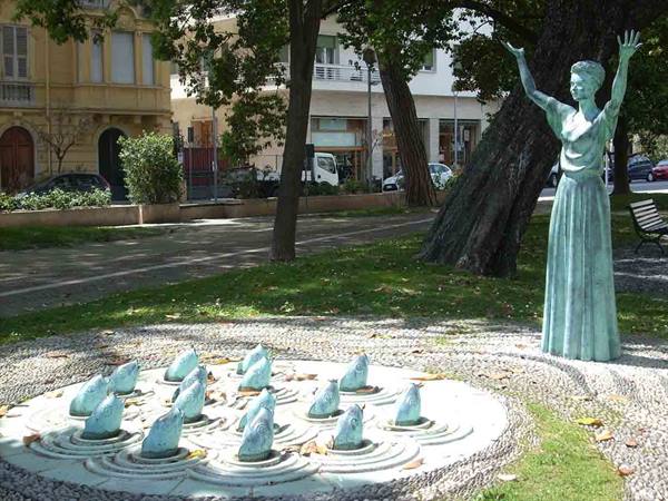 Bronze statue of woman with raised arms near bird sculptures in city park