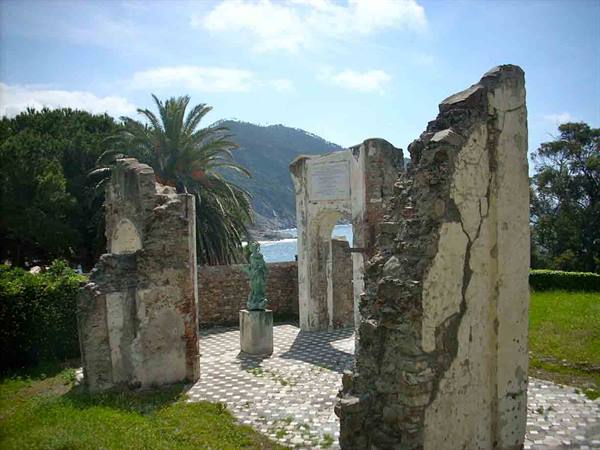 Weathered plastered ruins with arch, bronze statue, palm tree and sea