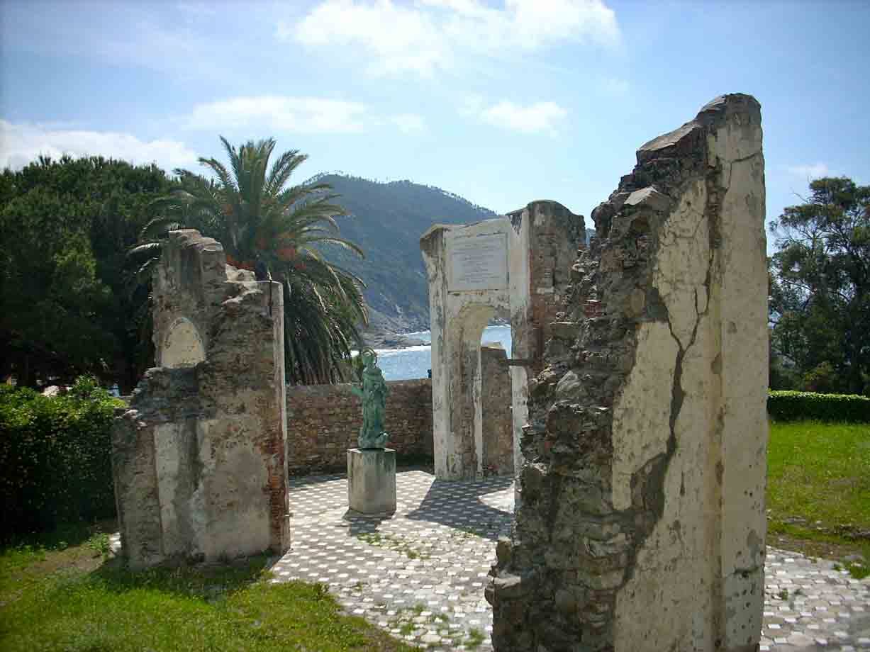 Rovine di muri intonacati con arco, statua in bronzo, palma e mare