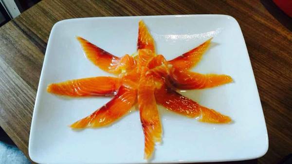 Smoked salmon slices arranged in a star pattern on white square plate