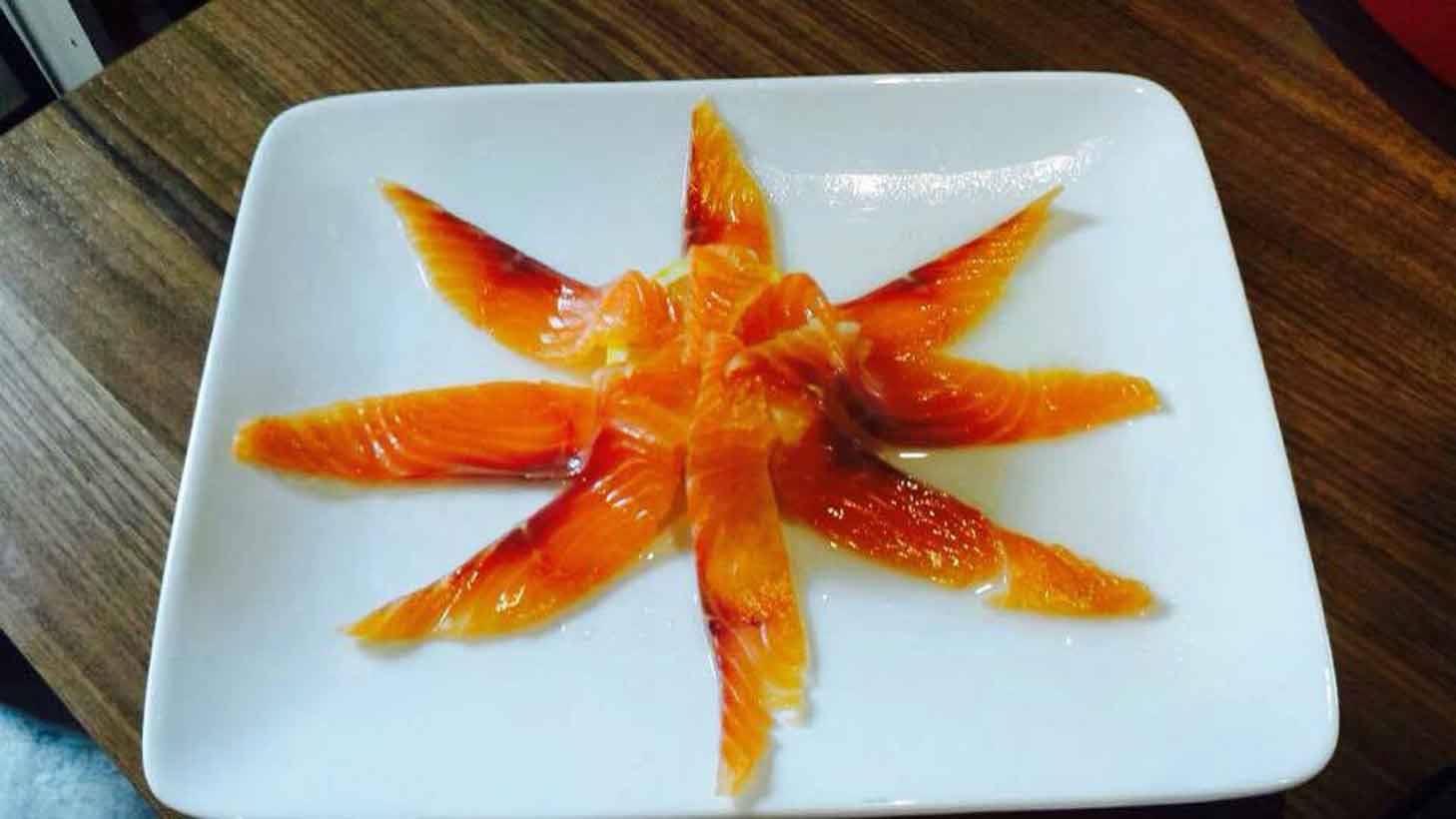 Fette di salmone affumicato disposte a stella su piatto bianco quadrato