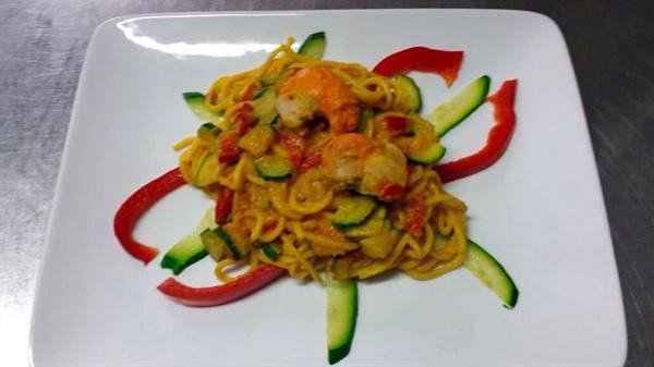 Spaghetti with shrimp and zucchini garnished with peppers on white plate
