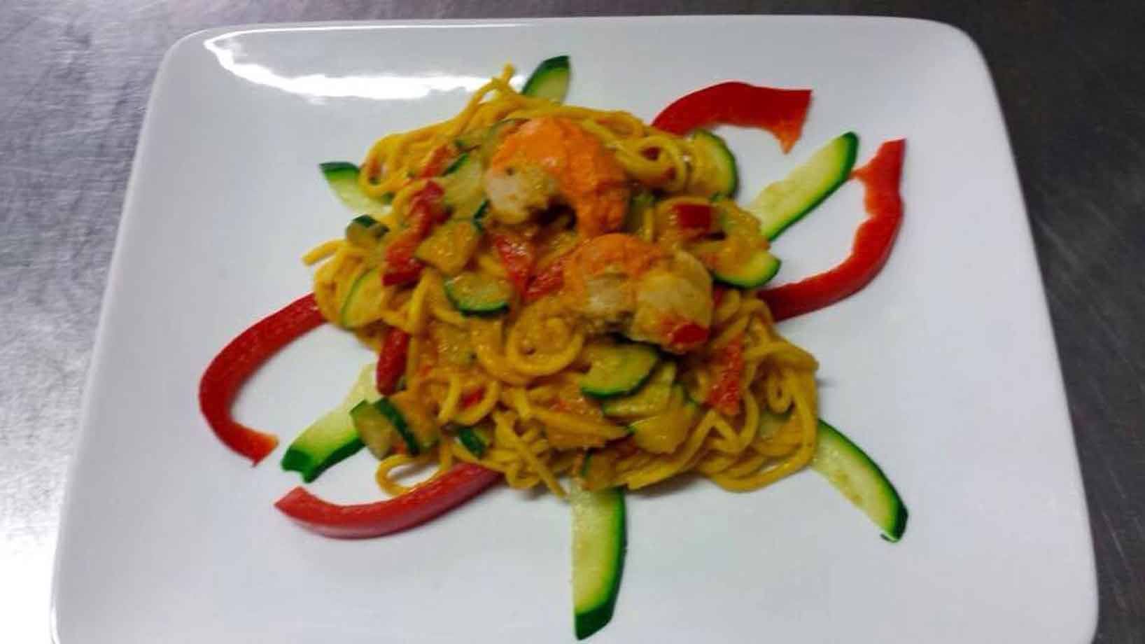 Spaghetti con gamberi e zucchine decorati con peperoni su piatto bianco