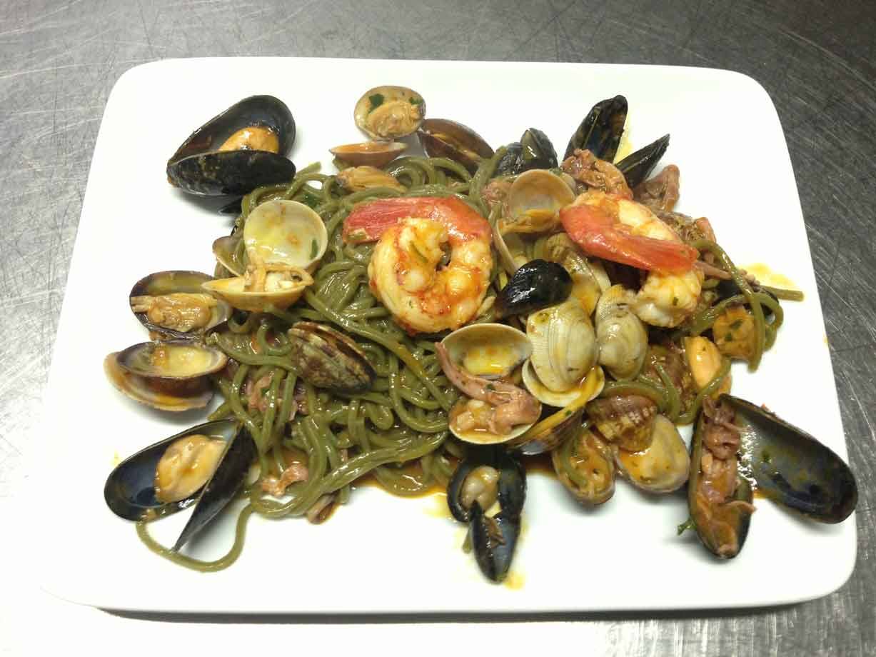 Spaghetti al nero di seppia con gamberi, cozze e vongole su piatto bianco
