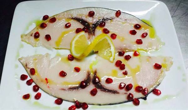 Raw swordfish slices with pomegranate seeds and lemon on white plate