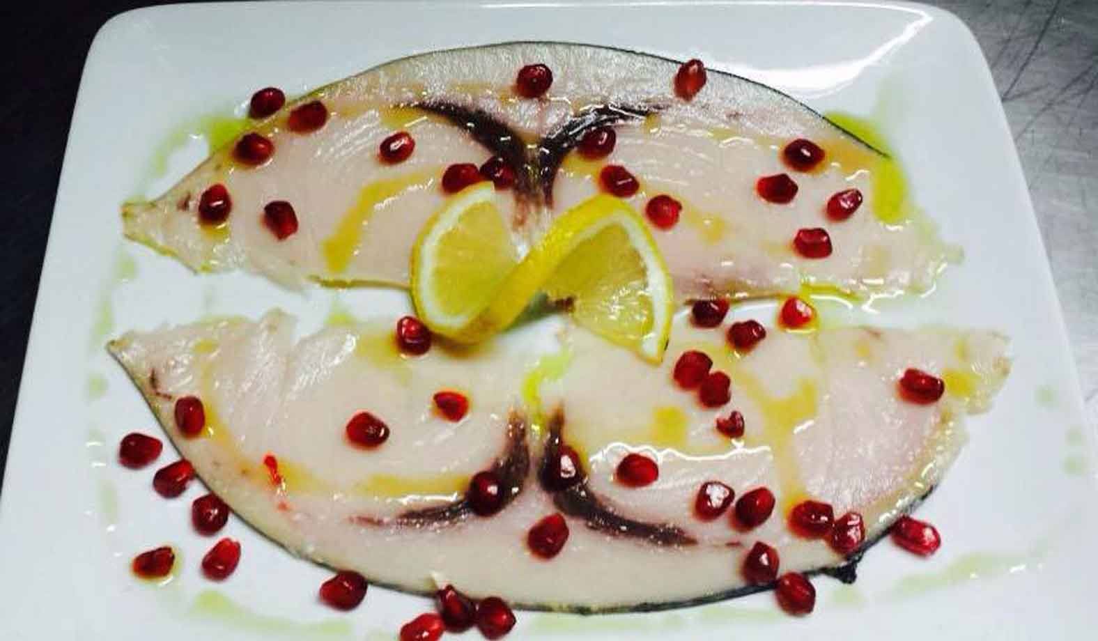 Fette di pesce spada crude con melagrana e limone su piatto bianco