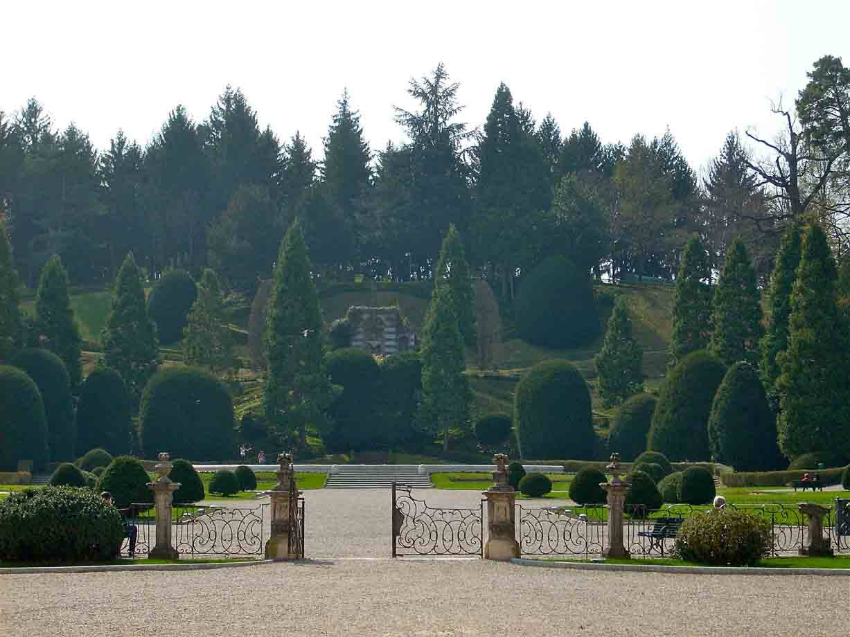 Cancello in ferro battuto su viale ghiaioso, giardini iconici, parco con conifere