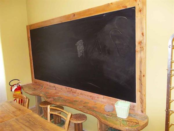 Black chalkboard framed in rustic wood above a carved counter, stools and fire extinguisher