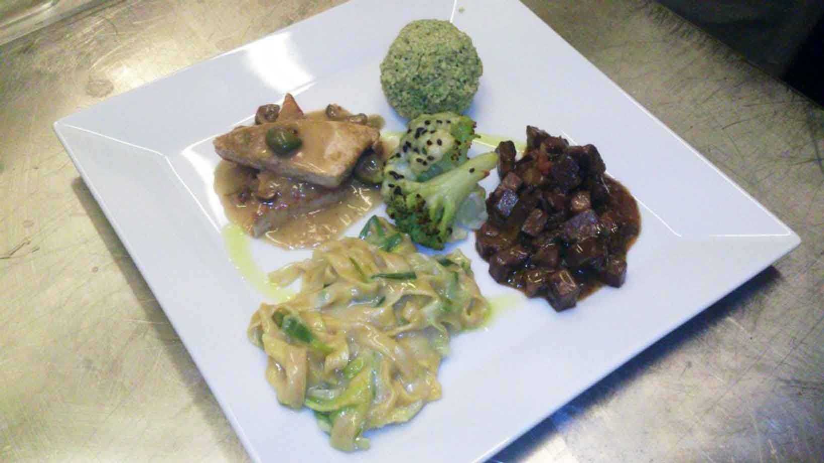 Piatto bianco quadrato su banco acciaio: tagliatelle, broccoli, carne in salsa e polpetta verde