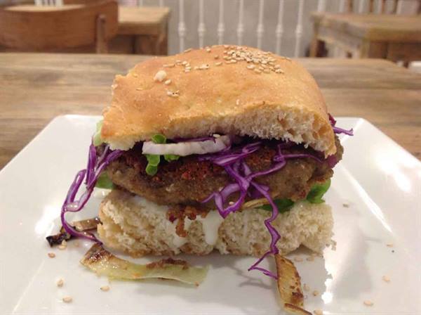 Burger with seeded bun, purple cabbage and onion on a white plate