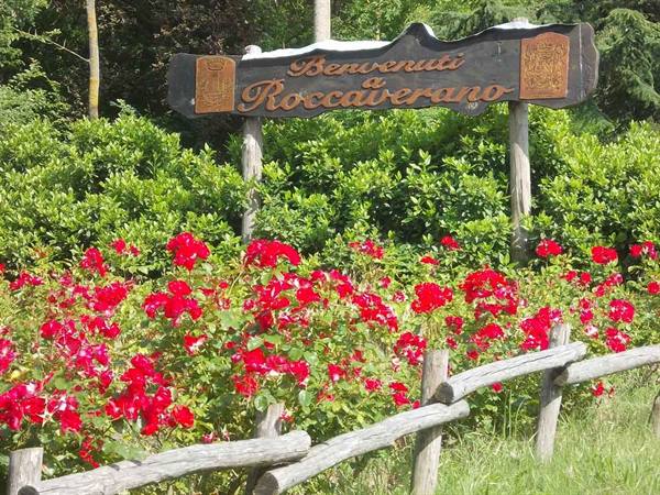 Wooden welcome sign at Roccaverano among red roses and rustic fence
