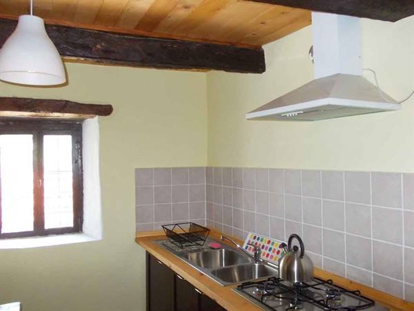 Rustic kitchen with wooden beams, steel sink, gas stove and kettle