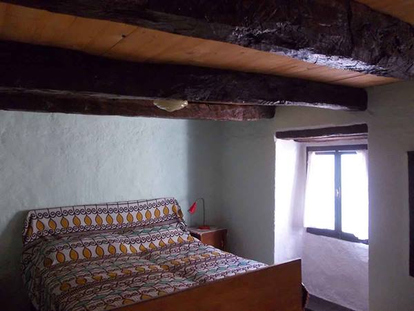 Bedroom with wooden bed, old ceiling beams and bright window