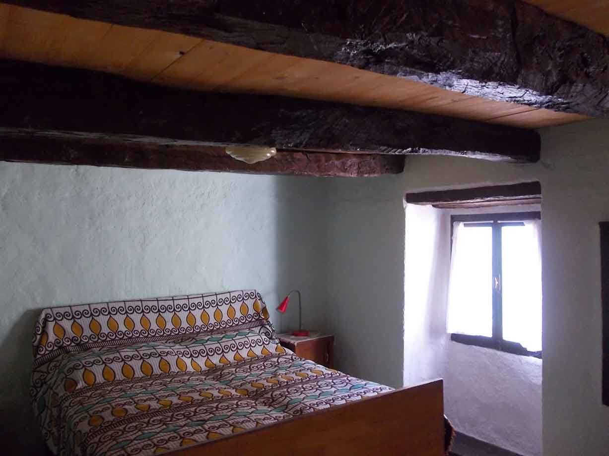 Camera con letto in legno, travi antiche al soffitto e finestra illuminata