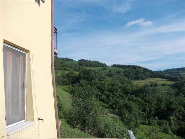 Yellow wall with curtained window overlooking green wooded hills under blue sky