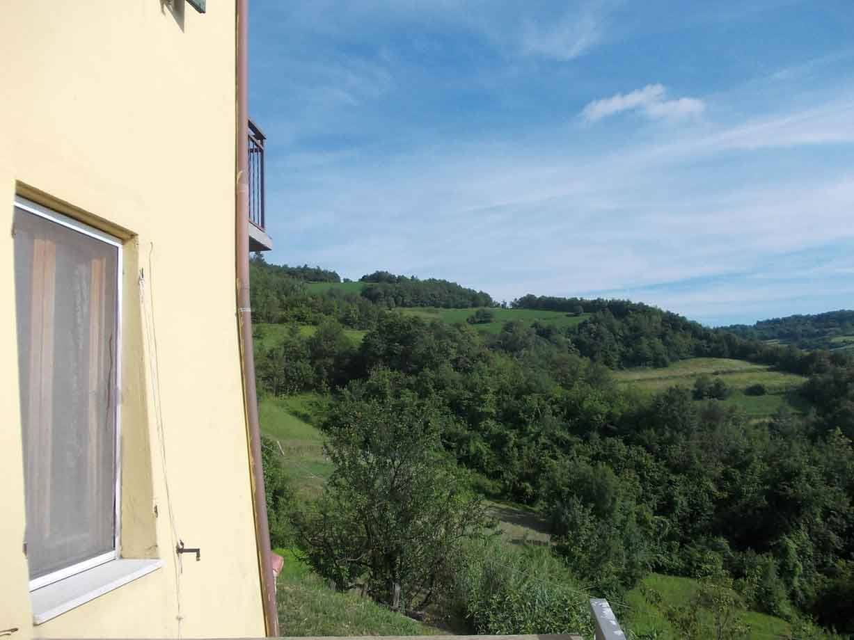 Muro giallo con finestra e tenda davanti alle colline verdi coperte di boschi