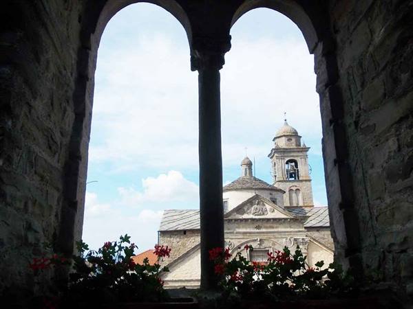 Stone church dome and bell tower seen through arched window, red flowers