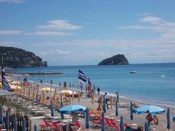 Beach with blue umbrellas and sunbeds, swimmers in the sea, Gallinara island behind