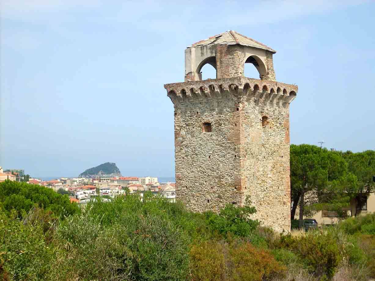 Torre antica in pietra con merlatura, macchia verde e Gallinara sullo sfondo
