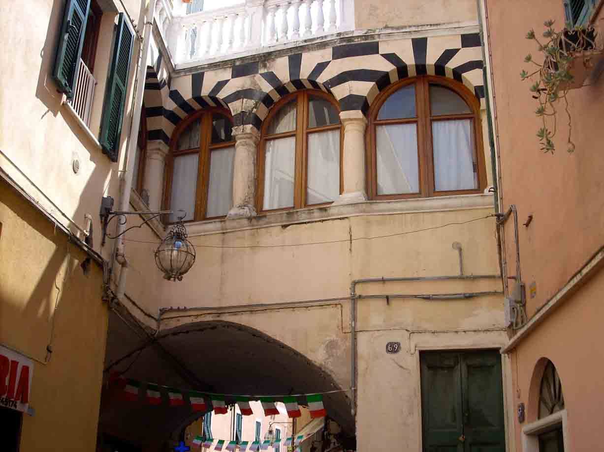 Palazzo a loggiato con archi bianchi e neri, lanterna e bandierine in un vicolo