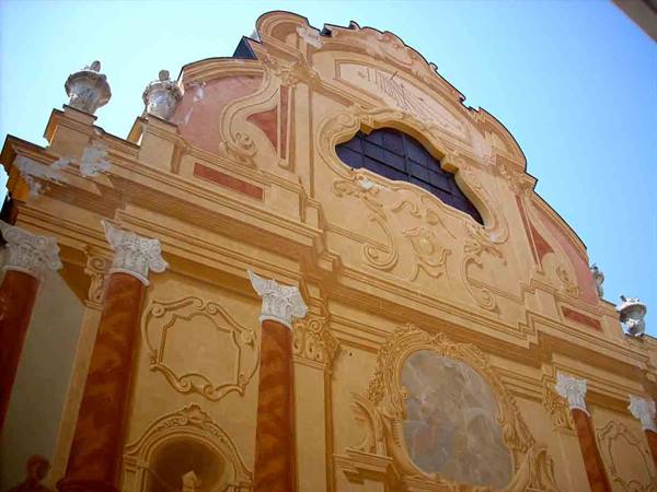 Ochre baroque facade with marble columns and lobed window, blue sky
