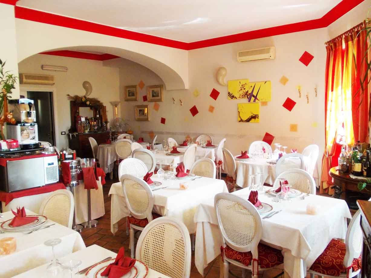 Sala ristorante apparecchiata con tovaglie bianche, sedie impagliate e addobbi rossi