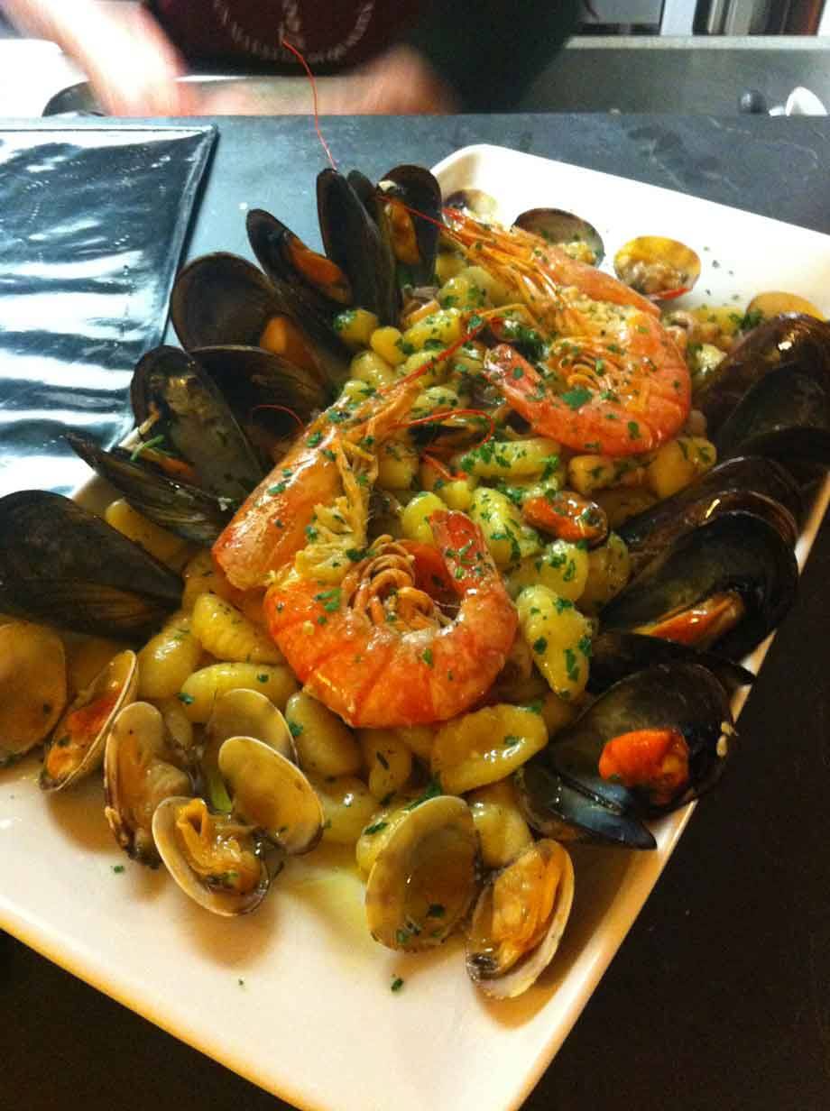 Gnocchi ai frutti di mare con gamberi, cozze e vongole su piatto bianco