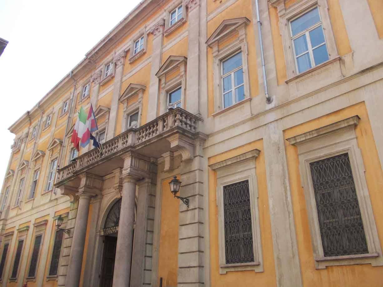 Palazzo giallo con colonne, bandiere italiane sul balcone, luce diurna