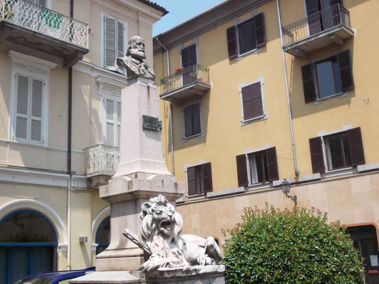 Monumento in pietra con busto in bronzo e leone scolpito tra palazzi colorati