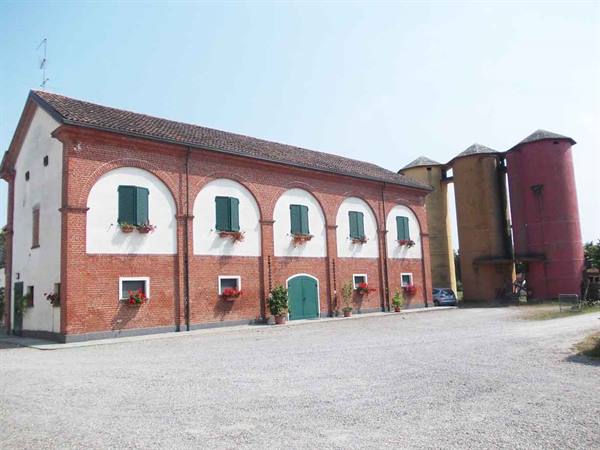 Red brick farmhouse with arches, colorful silos and gravel courtyard