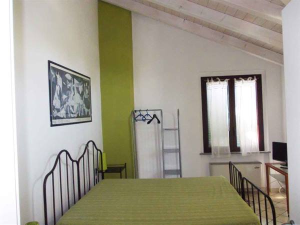 Bedroom with green iron bed, wooden beams and white curtains