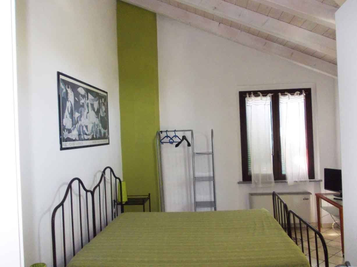 Camera con letto in ferro verde, travi in legno e tende bianche