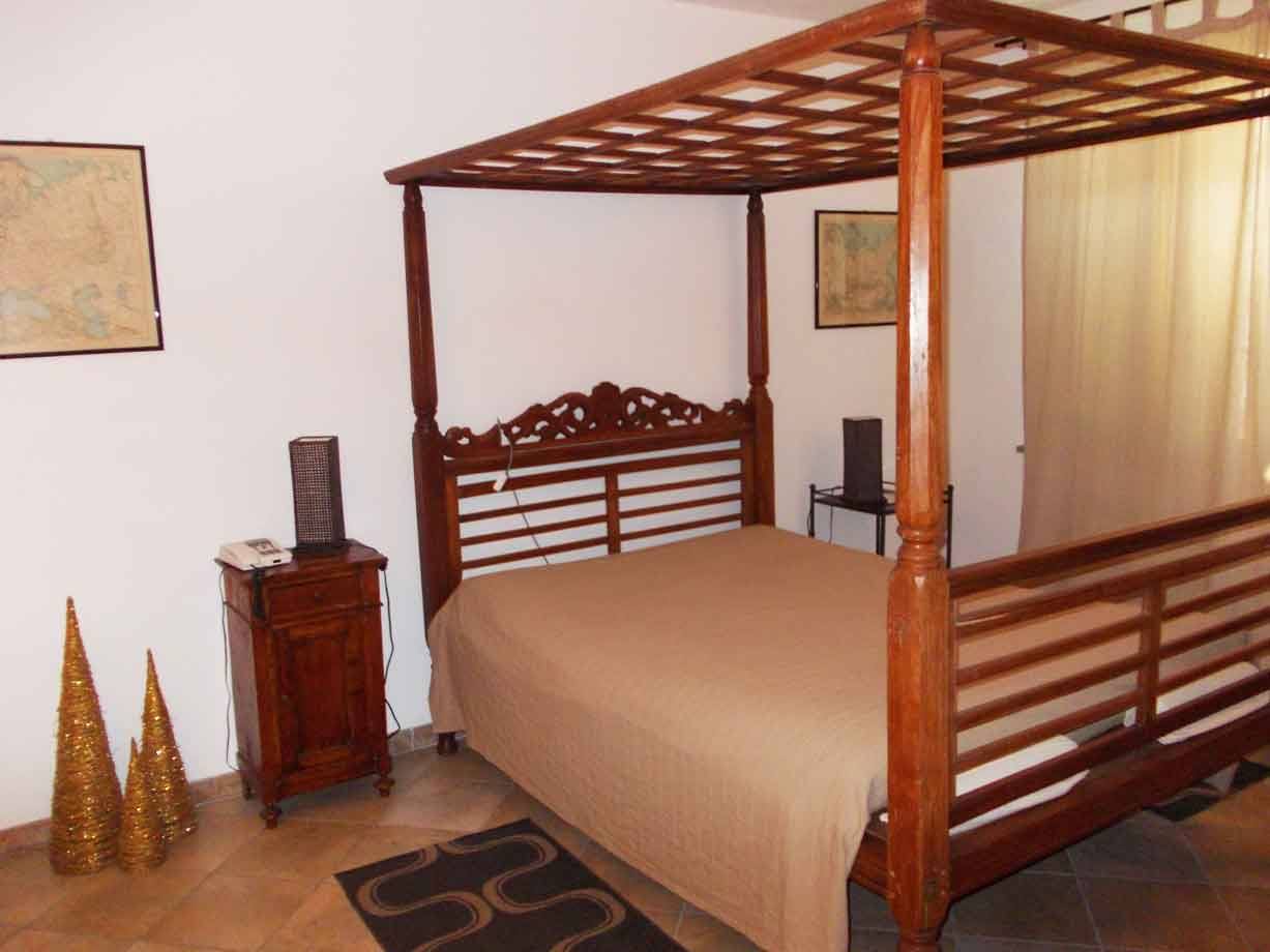 Camera da letto con letto a baldacchino in legno intagliato, comodino e cartine alle pareti
