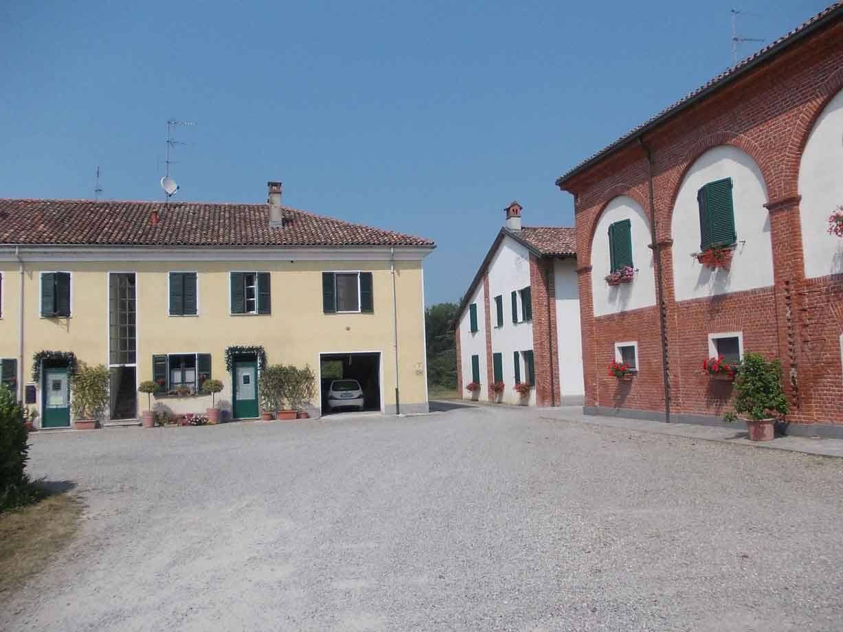 Cascina con case gialle e mattoni rossi, persiane verdi, cortile di ghiaia