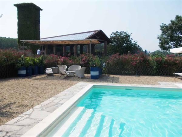 Turquoise pool with stone edge, white armchairs and wooden pavilion among flowers