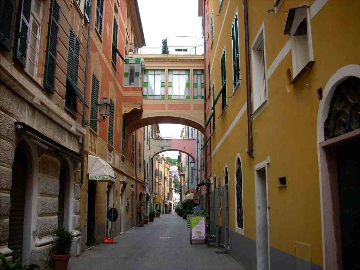 Via con archi dipinti in ocra e rosa a Genova, luce diffusa