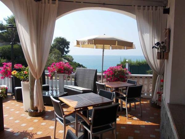 Terrace with wooden tables, umbrella, white curtains and flowers facing the sea