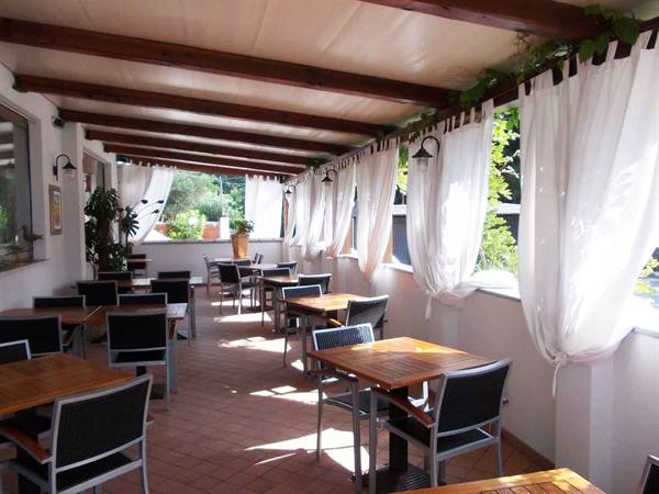 Covered restaurant dining area with wooden beams, white curtains and empty tables