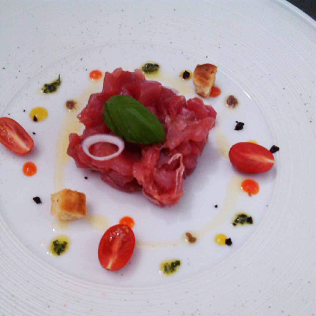Tartare di tonno crudo con basilico, pomodorini e crostini su piatto bianco