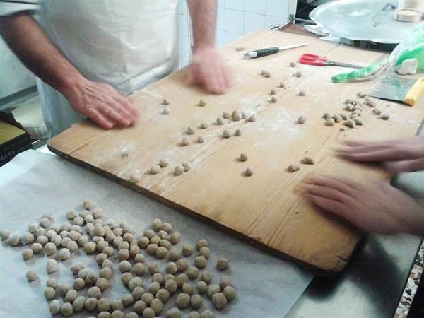 Hands shaping small dough balls on floured wooden board in kitchen
