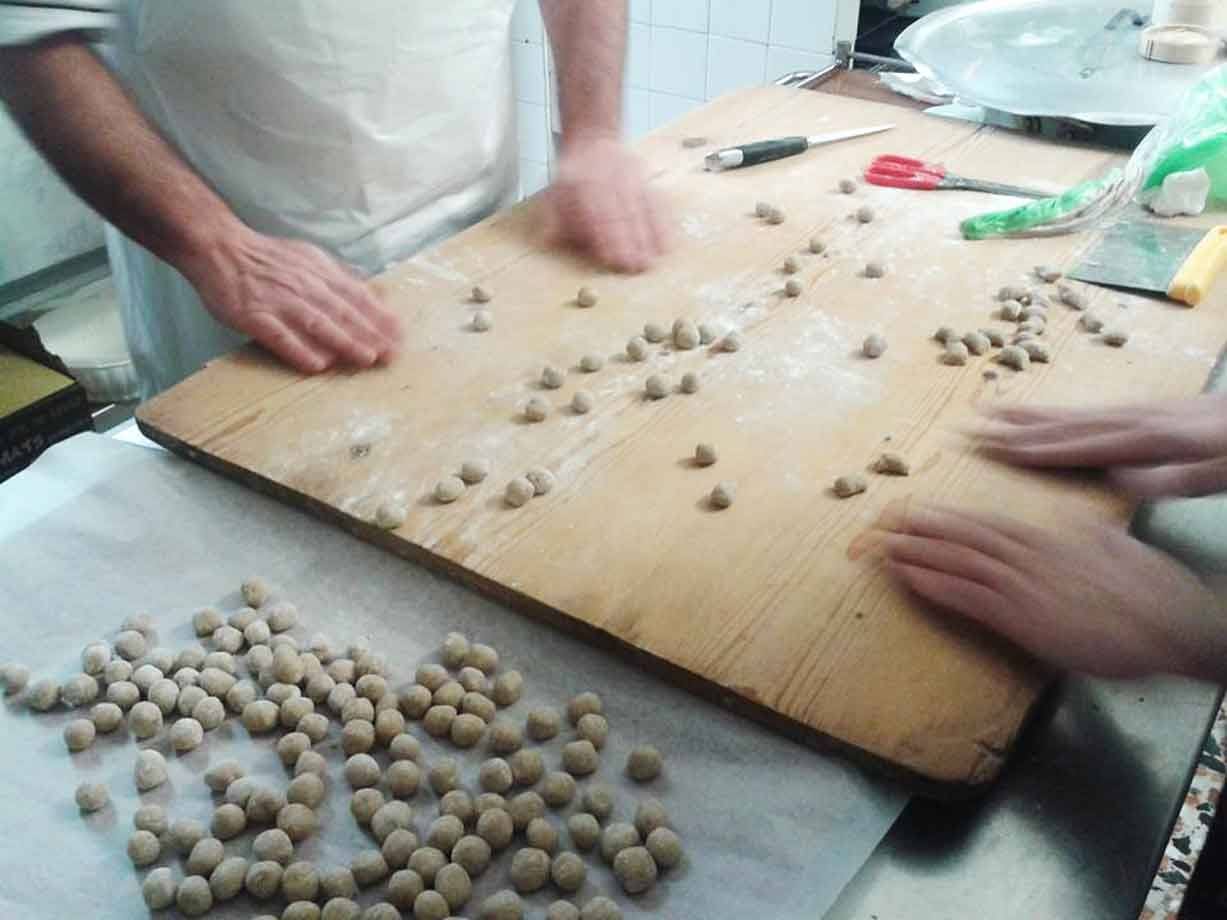 Mani formano palline di pasta su tavolo di legno infarinato in cucina