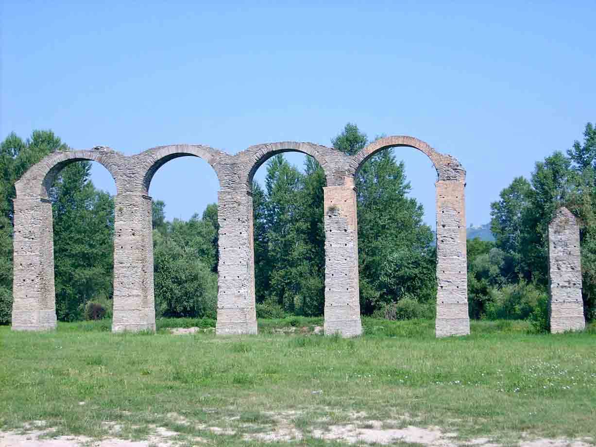 Arcate in mattoni di un antico acquedotto romano sull'erba, alberi verdi