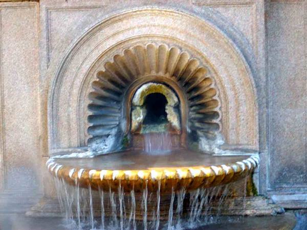 Stone fountain with carved shell, water overflowing from the brown basin