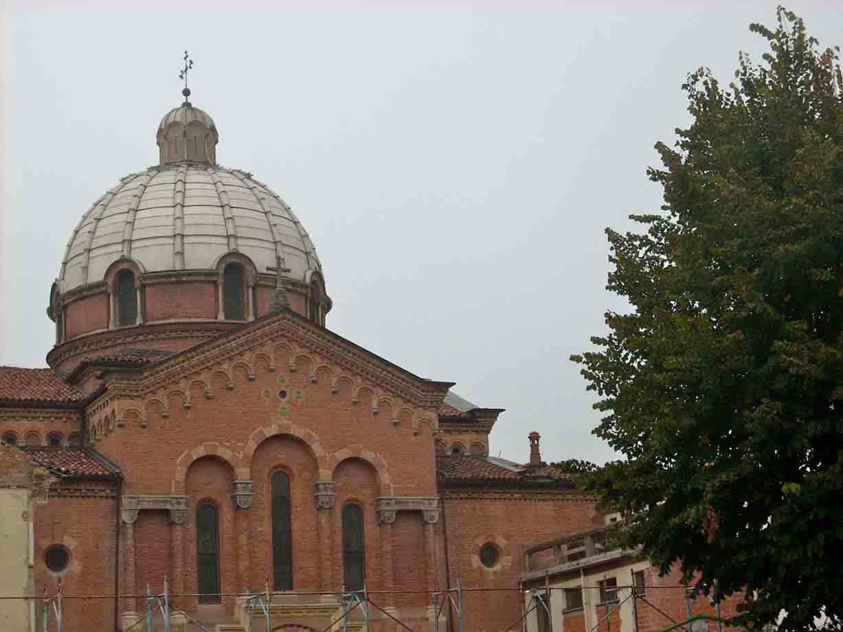 Chiesa in mattoni con cupola grigia sotto cielo nuvoloso, albero verde accanto
