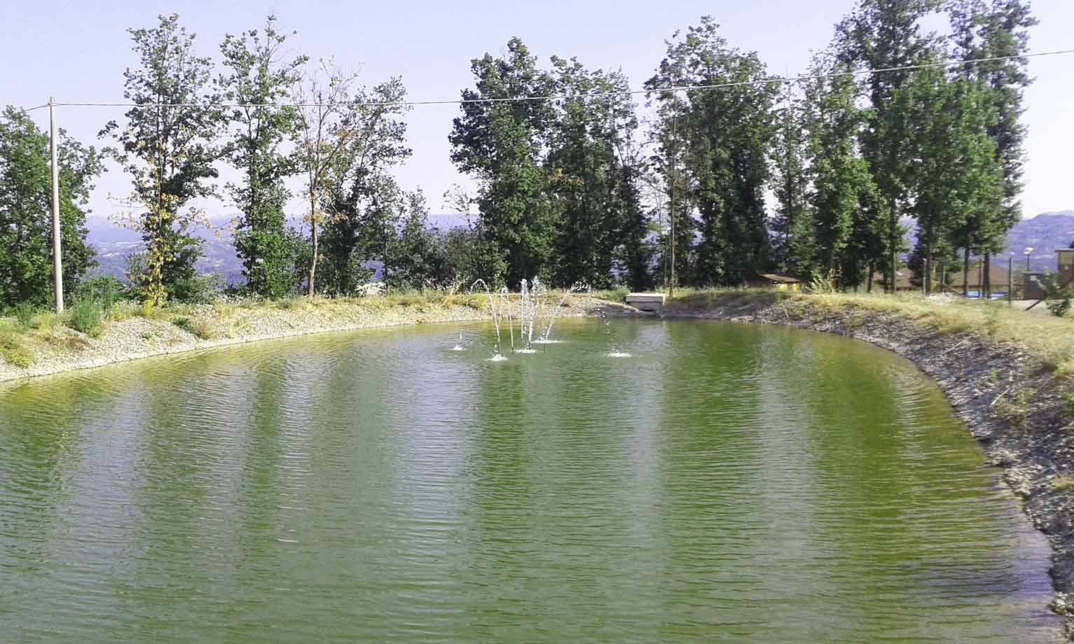 Laghetto verde con getti d'acqua circondato da alberi alti e colline