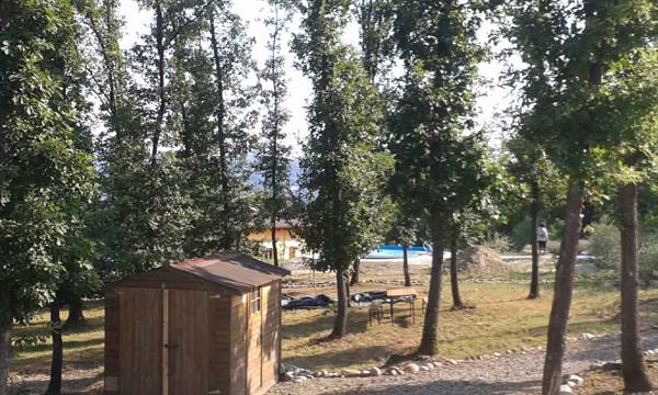 Small wooden shed among tall trees, a pool and picnic tables on the grass