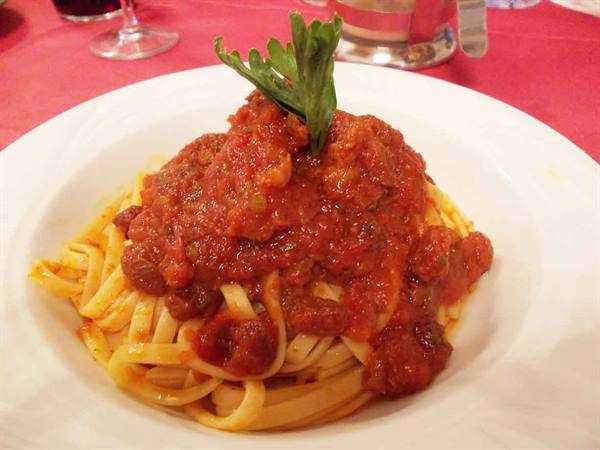 Tagliatelle with meat sauce in white plate, parsley garnish, red tablecloth