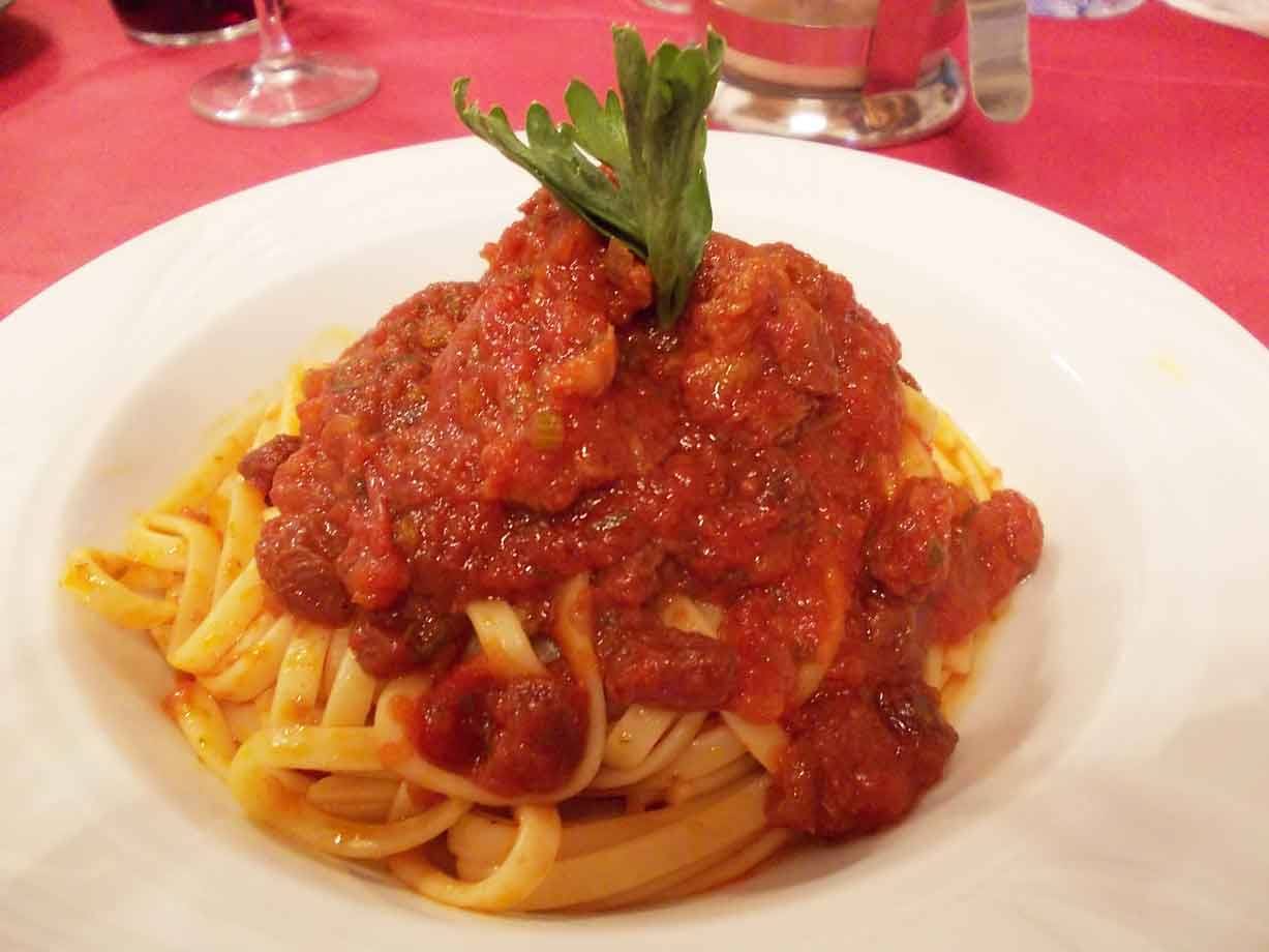 Tagliatelle al ragù in piatto bianco, guarnite con prezzemolo, tovaglia rossa