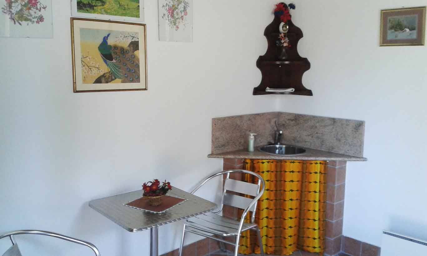 Lavello angolare in marmo con rubinetto, tenda gialla, tavolino e sedie metalliche