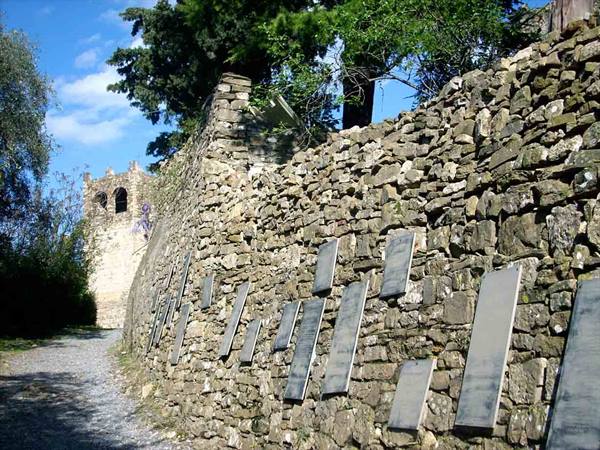 Stone wall with metal plaques along a path, medieval tower among trees